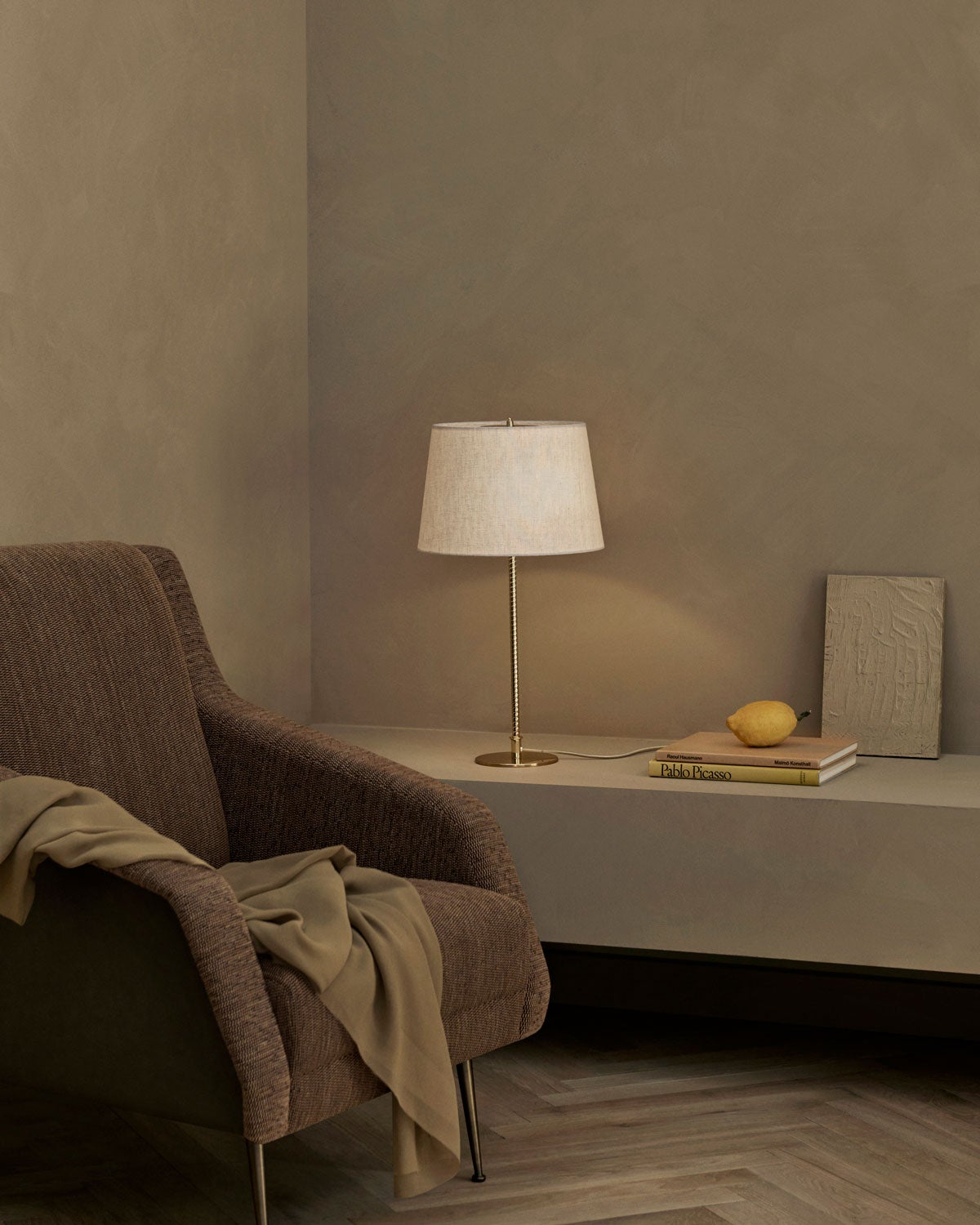 9205 Bordslampa från Gubi med lampskärm av canvas och lampfot i polerad mässing på en bänk i ett dämpat vardagsrum. 
